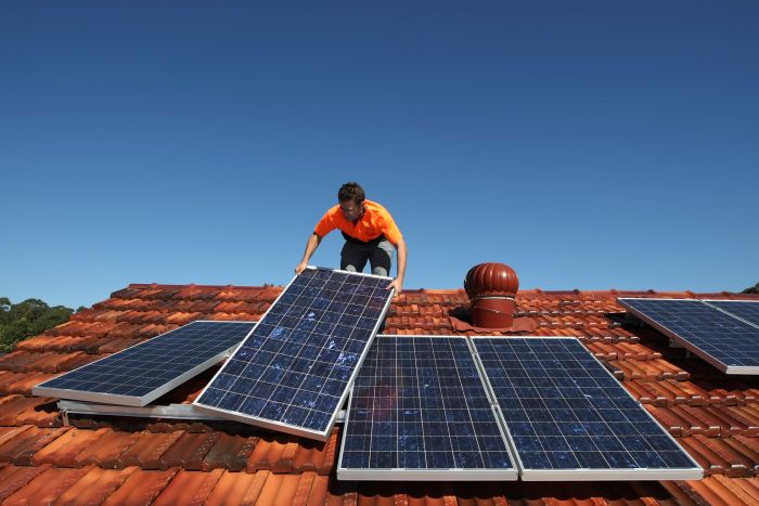 Solar panel installation A solar system installer adjusts solar panels on the roof of a house.