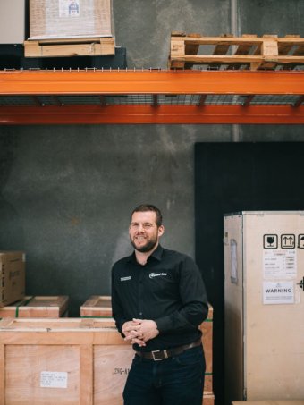 Andy McCarthy, of Gippsland Solar, in his warehouse A man leans against a crate in a warehouse