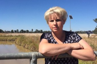 Natalie Akers A woman with short blond hair leaning against a fence, with an irrigation channel in the background.